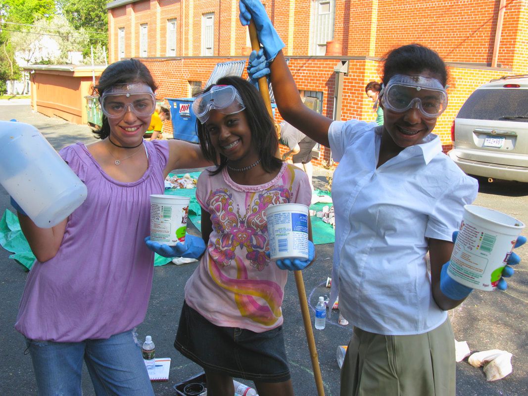 Three girls posing playfully while holding containers and nets in an urban setting.
